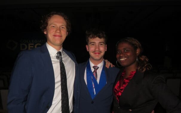 Three Avila University students dressed in professional attire smiling together at a Collegiate DECA event.